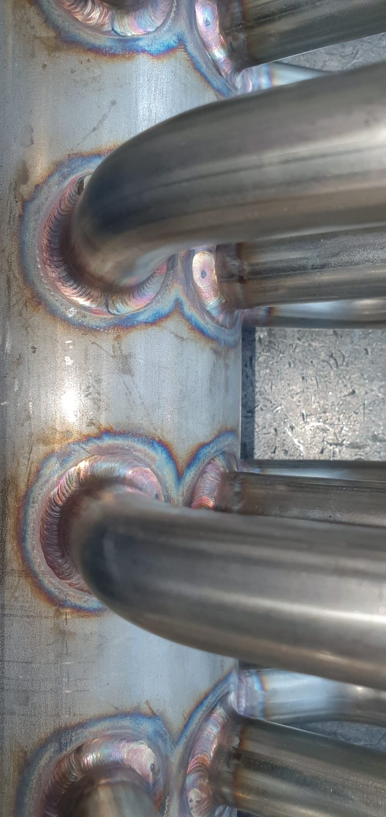 Szczegółowe ujęcie spawanych rur ze stali nierdzewnej, widoczne tęczowe przebarwienia na spoinach, świadczące o wysokiej temperaturze podczas spawania.