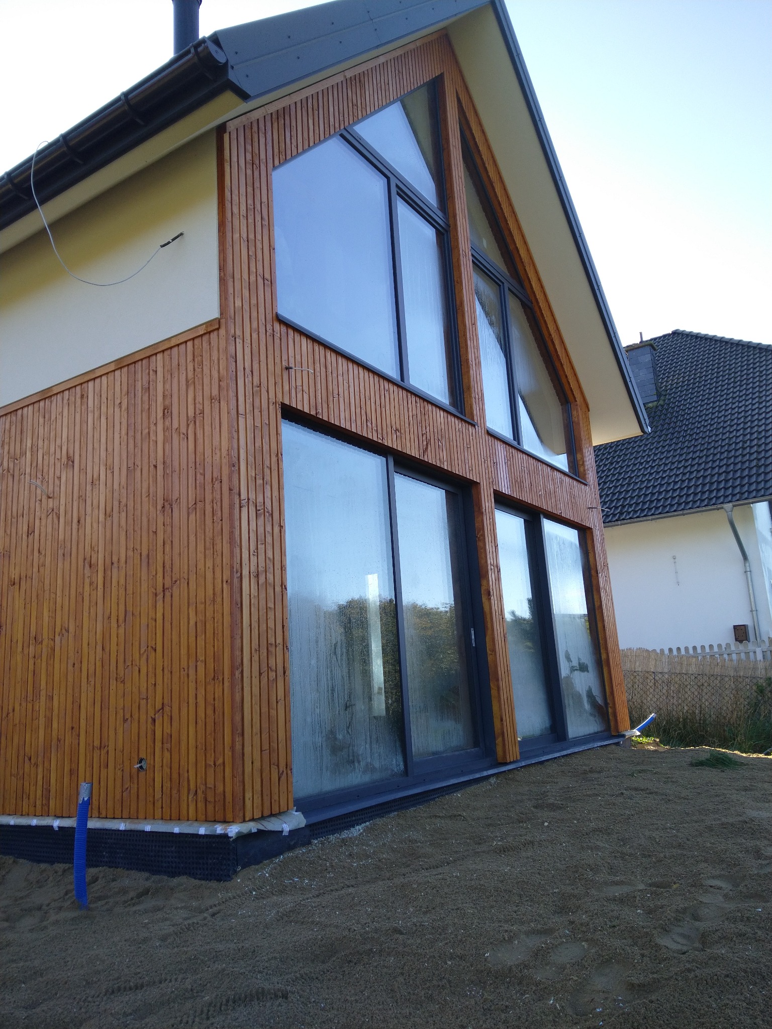 Nowoczesny dom z drewnianą elewacją i dużymi oknami, widok z zewnątrz na niedawno wyrównany teren.