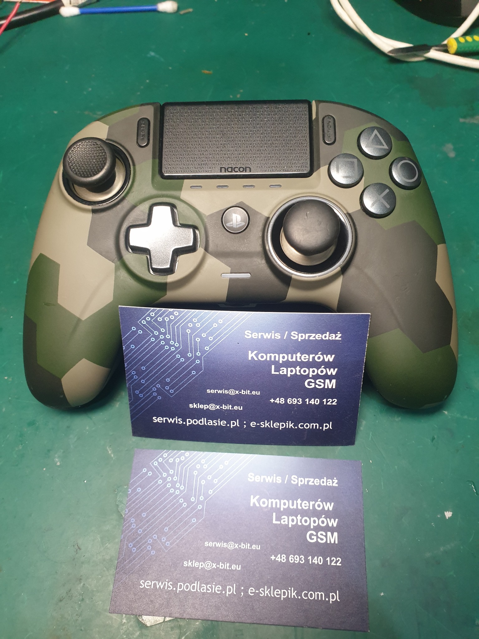 Pad Nacon w kamuflażu na zielonym tle, obok wizytówki serwisu komputerowego z adresem serwisu.podlasie.pl.