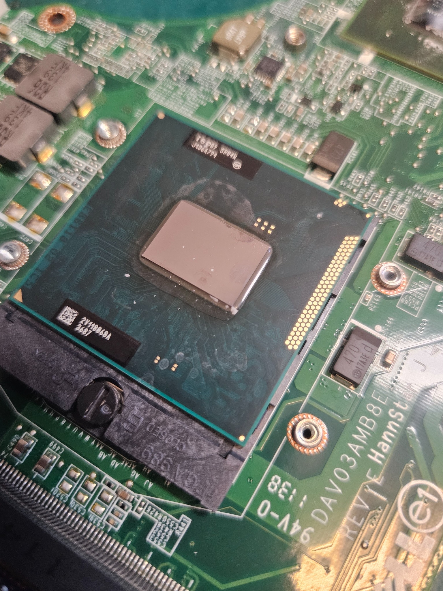 Otwarty laptop z widocznym procesorem i pastą termoprzewodzącą, ukazujący skomplikowaną budowę płyty głównej z elementami elektronicznymi.