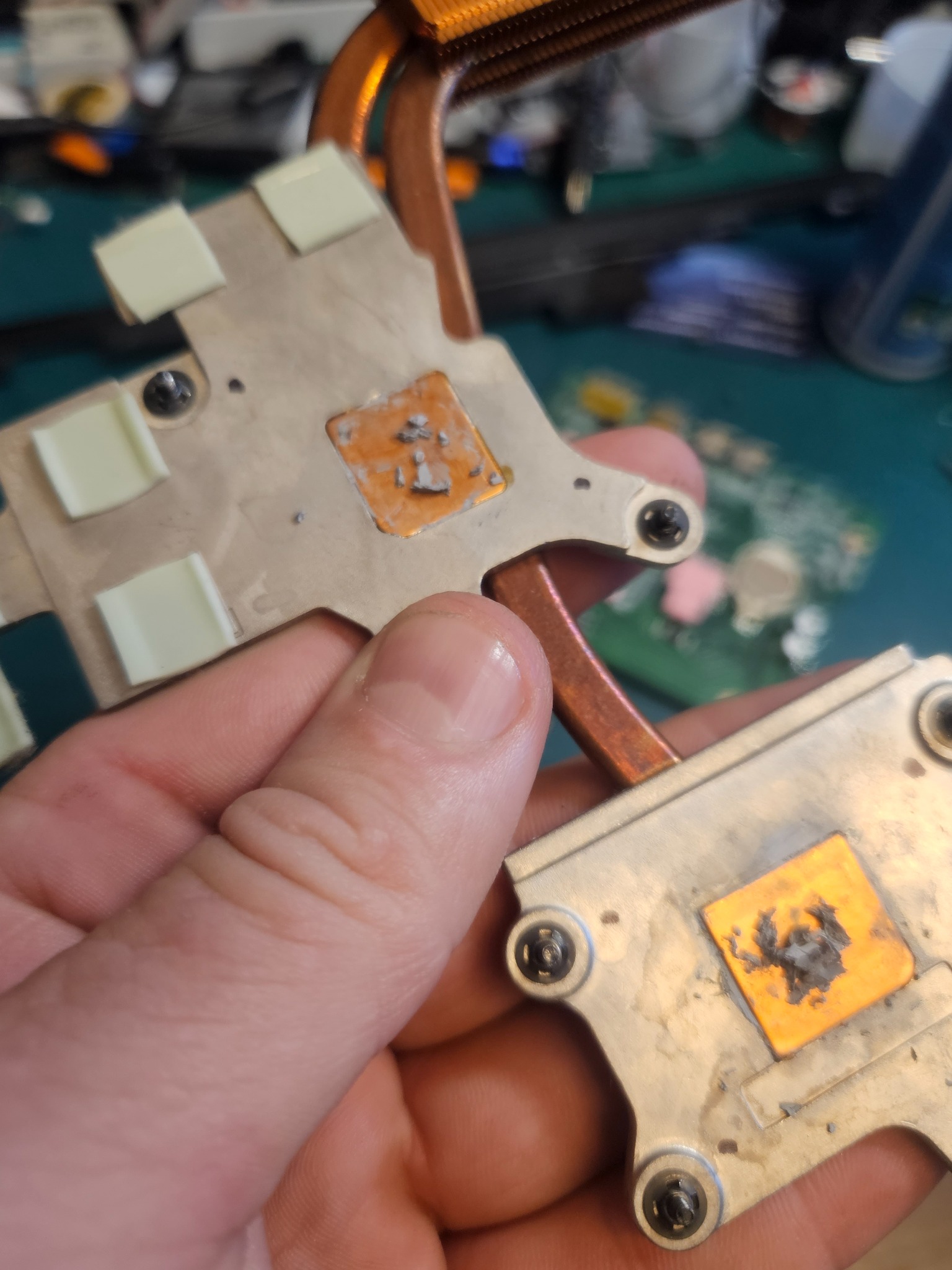 Używany radiator procesora z resztkami pasty termoprzewodzącej i naklejek termicznych, trzymany w dłoni, widoczne ślady użytkowania i miedziane ciepłowody.