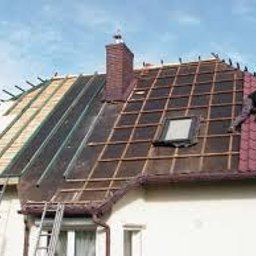 Usługi blacharsko dekarskie Łukasz Maciejowski - Demontaż starego pokrycia dachowego i montaż nowego pokrycia z blachodachówki w kolorze bordowym. Widoczny fragment dachu z oknem dachowym, rusztowanie oraz dwóch dekarzy pracujących na różnych...