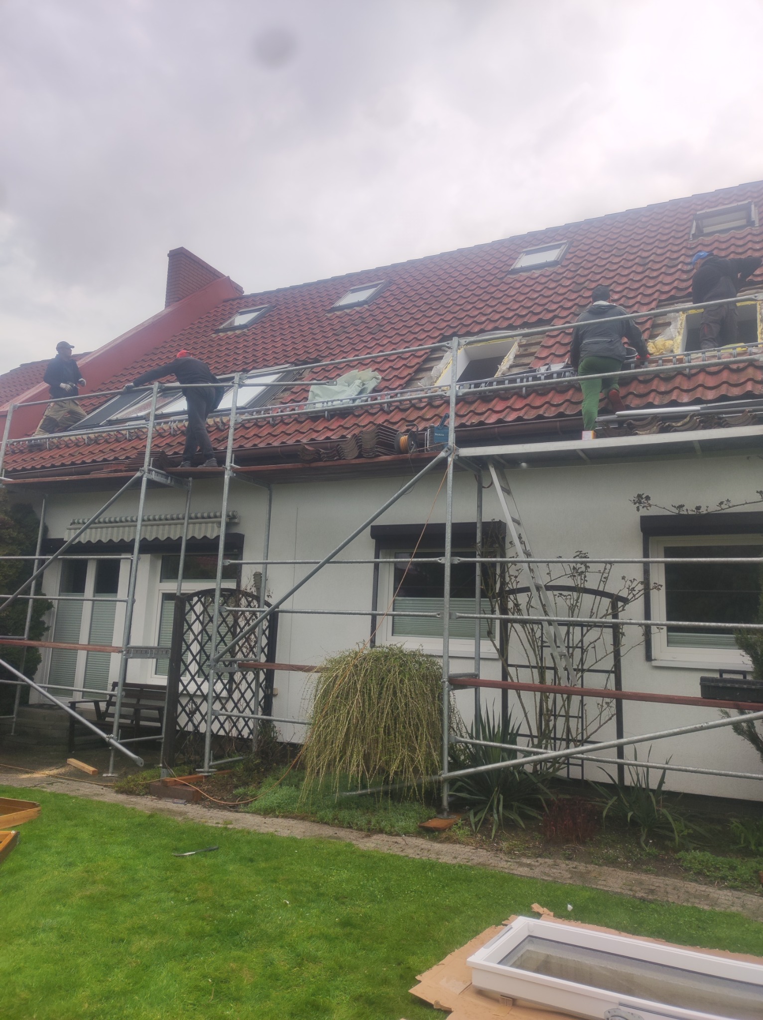 Ekipa dekarzy z Raciborza na rusztowaniu podczas montażu okien dachowych w trakcie prac na dachu pokrytym czerwoną dachówką.