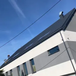 Prace dekarskie w Krakowie: Robotnicy na dachu nowoczesnego, dwukolorowego domu z nowym, ciemnoszarym pokryciem i oknami dachowymi, widok z dołu pod kątem.