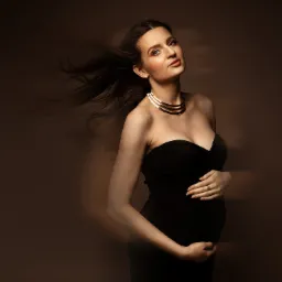 Portret kobiety w czarnej sukni, trzymającej ręce na brzuchu, z rozwianymi włosami i złotym naszyjnikiem na brązowym tle.