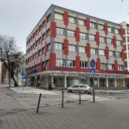 Nowoczesny budynek biurowy z elewacją w szaro-czerwone pasy, widoczny z poziomu ulicy z przejściem dla pieszych i znakami drogowymi.