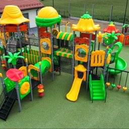 Big Toys Elżbieta Zygaryn - Duży, nowoczesny zestaw zabawowy z żółtymi zjeżdżalniami, zielonymi tunelami, siatkami i interaktywnymi panelami na zielonej nawierzchni bezpiecznej, obok budynku.