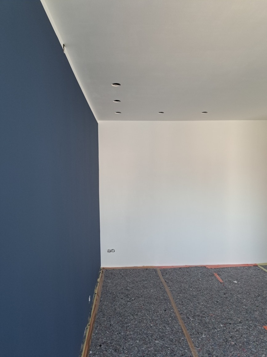 Pomieszczenie po malowaniu ścian na biało i granatowo, z przygotowanym podłożem pod wylewkę i zamontowanymi punktami oświetleniowymi w suficie.