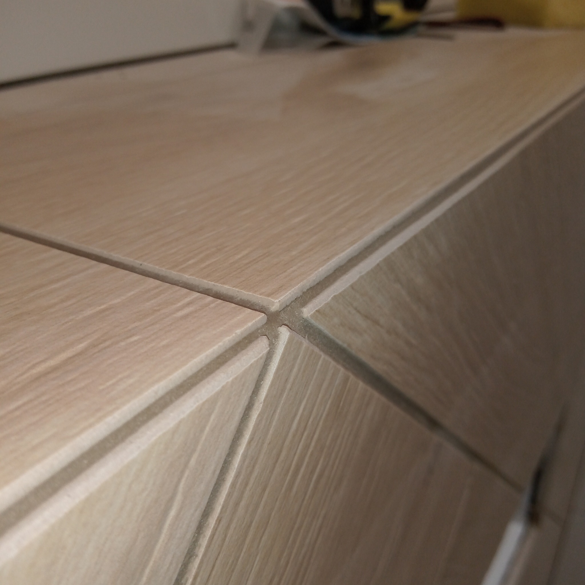 Bliski kadr na fragment szafki łazienkowej wykończonej płytkami imitującymi drewno, z widocznymi fugami i subtelnym wzorem słojów.