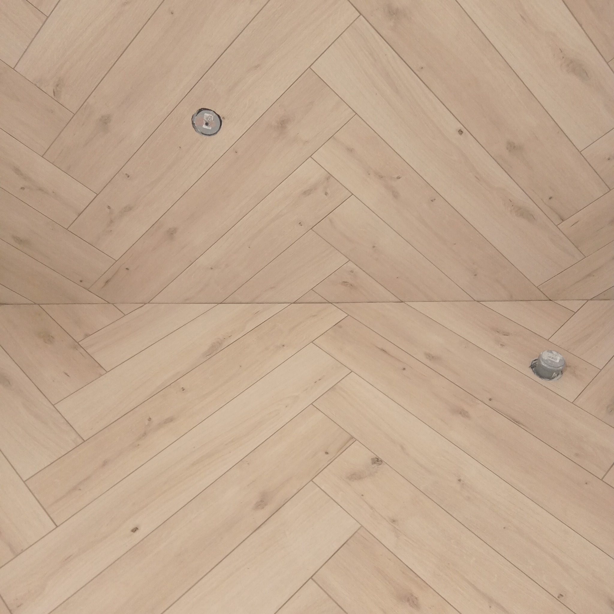 Jasna podłoga ułożona w jodełkę z widocznymi otworami po instalacji elektrycznej.