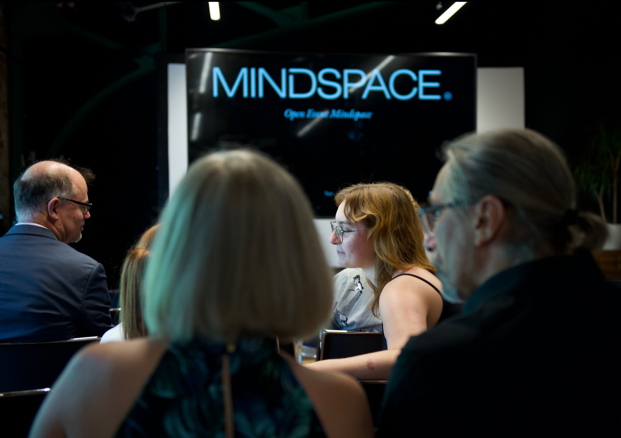 Uczestnicy konferencji w sali z logo Mindspace na ekranie, widok zza pleców.