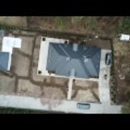 M&S Garden - Widok z drona na posesję z domem w trakcie prac ziemnych pod przyszły ogród. Wykopane rowy sugerują plan nasadzeń lub instalację systemu nawadniającego. Szara kostka brukowa ułożona wokół domu...