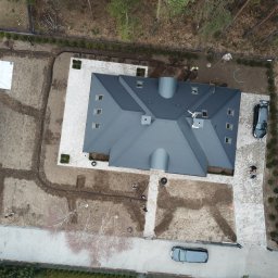 M&S Garden - Widok z lotu ptaka na posesję w trakcie prac ogrodowych: ułożona kostka brukowa wokół domu, przygotowane rabaty, widoczne zarysy przyszłych nasadzeń, częściowo rozłożona folia na gruncie, samochody...