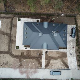 M&S Garden - Widok z drona na posesję w Otwocku w trakcie prac ogrodowych, widoczny dom z szarym dachem, ułożona kostka brukowa, przygotowany teren pod trawnik i system nawadniania, pracownicy w żółtych...