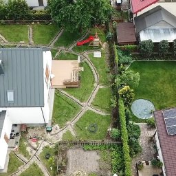 M&S Garden - Widok z góry na ogród w trakcie instalacji systemu nawadniania, widoczne wykopy pod rury, trawnik, taras, plac zabaw i panele słoneczne na dachu sąsiedniego domu.