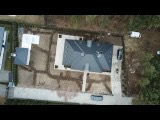 Widok z drona na posesję z domem w trakcie prac ziemnych pod przyszły ogród. Wykopane rowy sugerują plan nasadzeń lub instalację systemu nawadniającego. Szara kostka brukowa ułożona wokół domu...