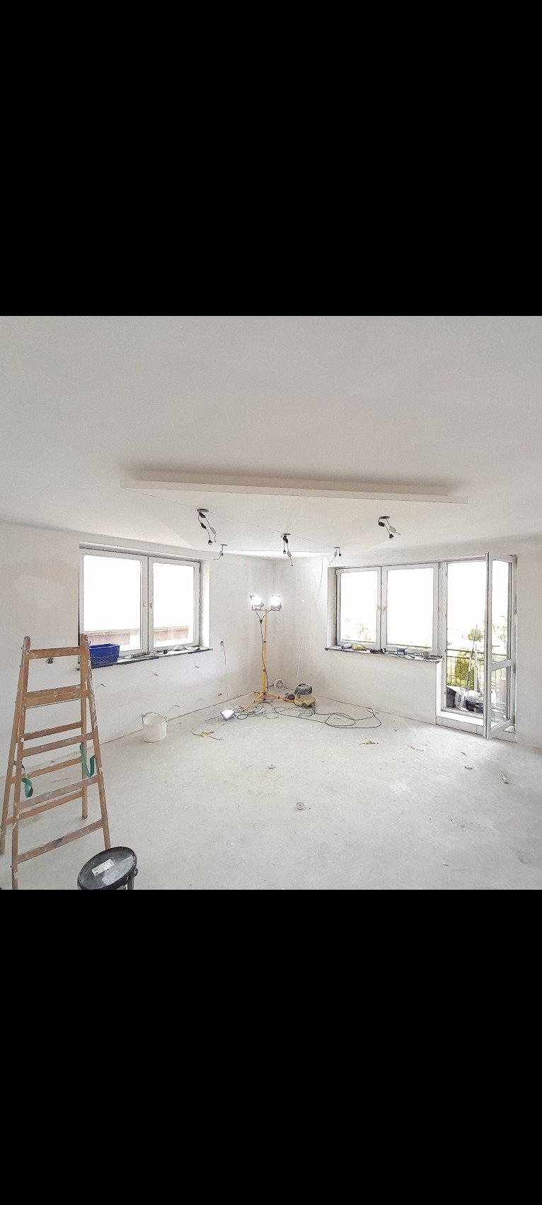 Wnętrze w trakcie prac przygotowawczych do wykończenia, widoczna drabina, lampy robocze oraz ściany po wstępnym wyrównaniu.