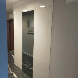 Biała szafa wnękowa z przesuwnymi drzwiami, marmurowa podłoga, widok na wnętrze z obrazem na ścianie.