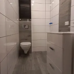 Nowoczesna łazienka z białymi, błyszczącymi płytkami, grzejnikiem drabinkowym, podwieszaną toaletą i szafką umywalkową z szufladami.