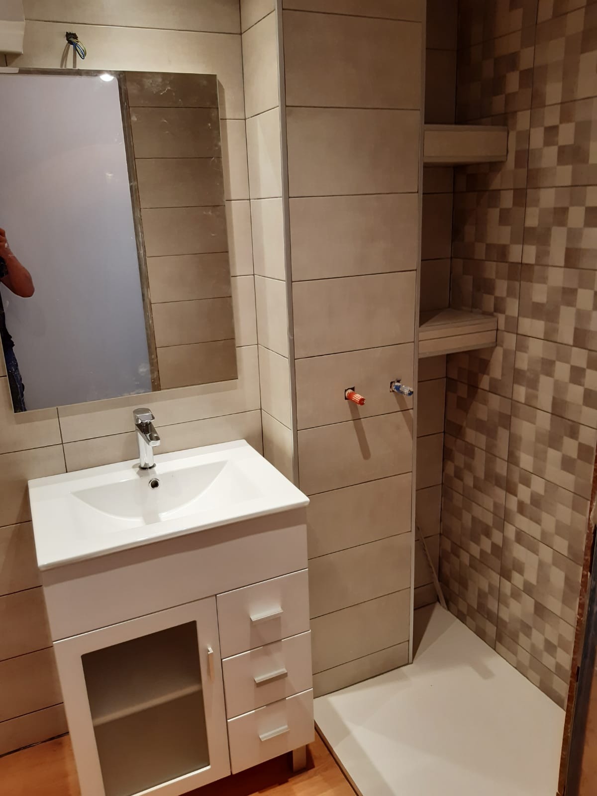 Wykończona łazienka z umywalką na szafce, lustrem i półkami w zabudowie, wyłożona beżowymi i brązowymi płytkami w neutralnych odcieniach.