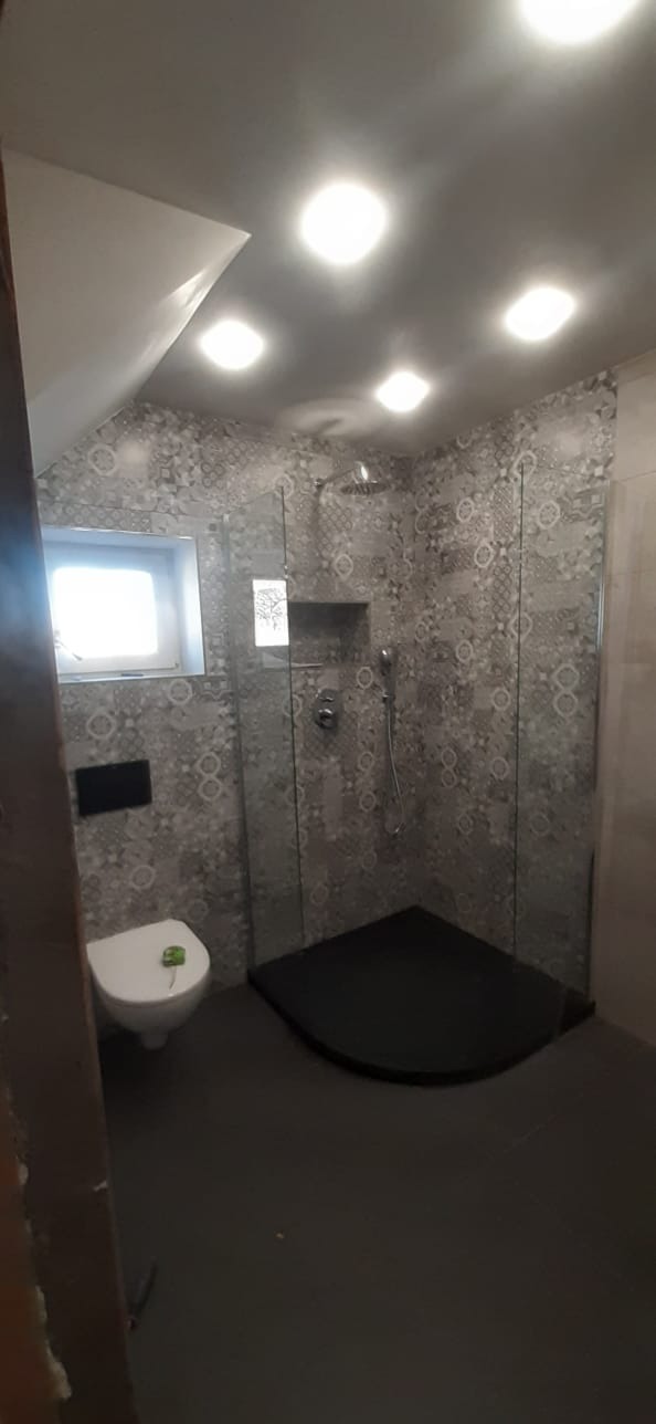 Wykończona łazienka na poddaszu z kabiną prysznicową bez brodzika, szarymi płytkami wzorzystymi, toaletą i oknem