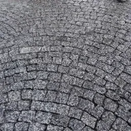 Szara kostka granitowa ułożona w łukowaty wzór, widok z góry, z delikatną teksturą kamienia.