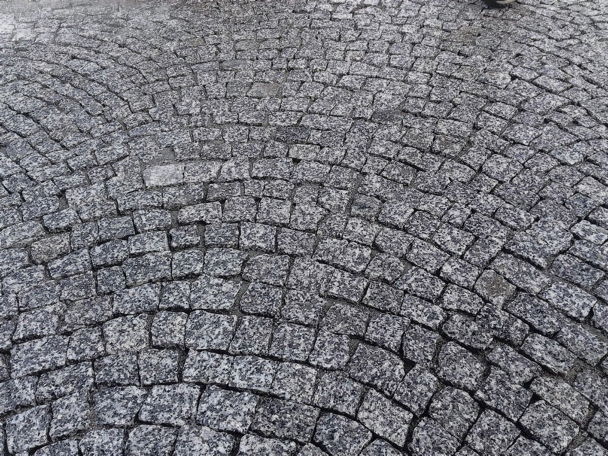 Szara kostka granitowa ułożona w łukowaty wzór, widok z góry, z delikatną teksturą kamienia.
