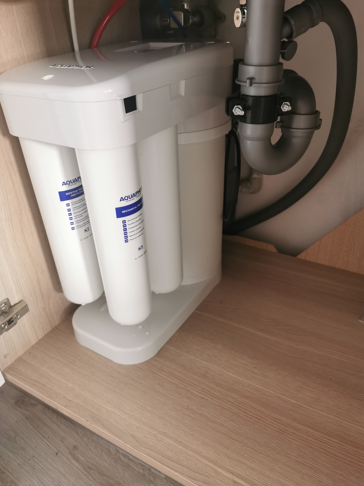 Filtr do wody Aquaphor K5 zamontowany pod zlewem, widoczne rury doprowadzające i odprowadzające wodę oraz syfon.