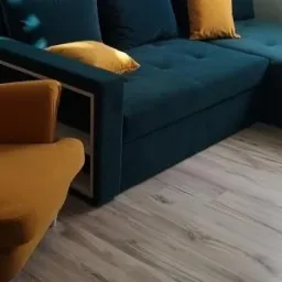 Narożnik tapicerowany w odcieniach granatu i musztardowej żółci z poduszkami dekoracyjnymi, widoczny fragment fotela w kolorze musztardowym, Sosnowiec.