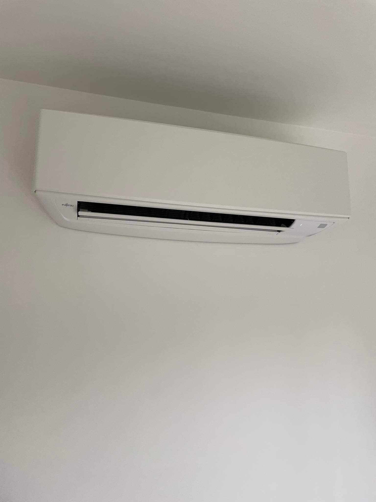 Biała jednostka wewnętrzna klimatyzacji Fujitsu zamontowana na gładkiej, jasnej ścianie, widoczna z przodu.
