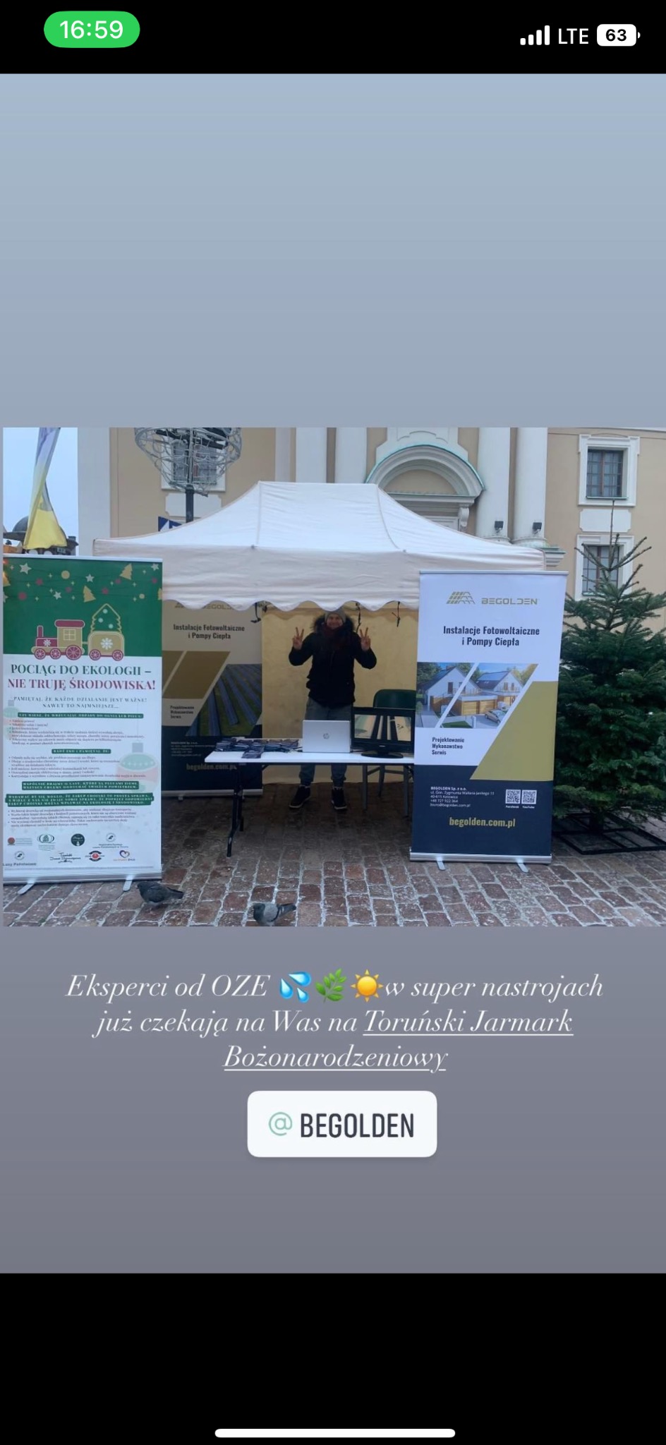 Stoisko firmy z Torunia na Jarmarku Bożonarodzeniowym, prezentujące ofertę instalacji fotowoltaicznych i pomp ciepła. Na bannerach logo firmy Begolden. Pracownik pozuje z dwoma palcami w górze.