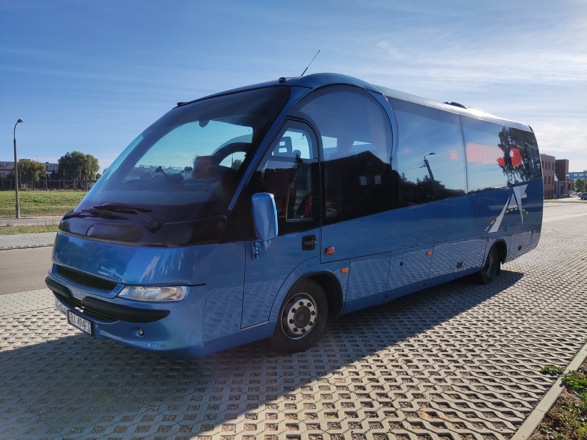 Niebieski autokar turystyczny zaparkowany na placu z ażurowej kostki, widoczny numer rejestracyjny.