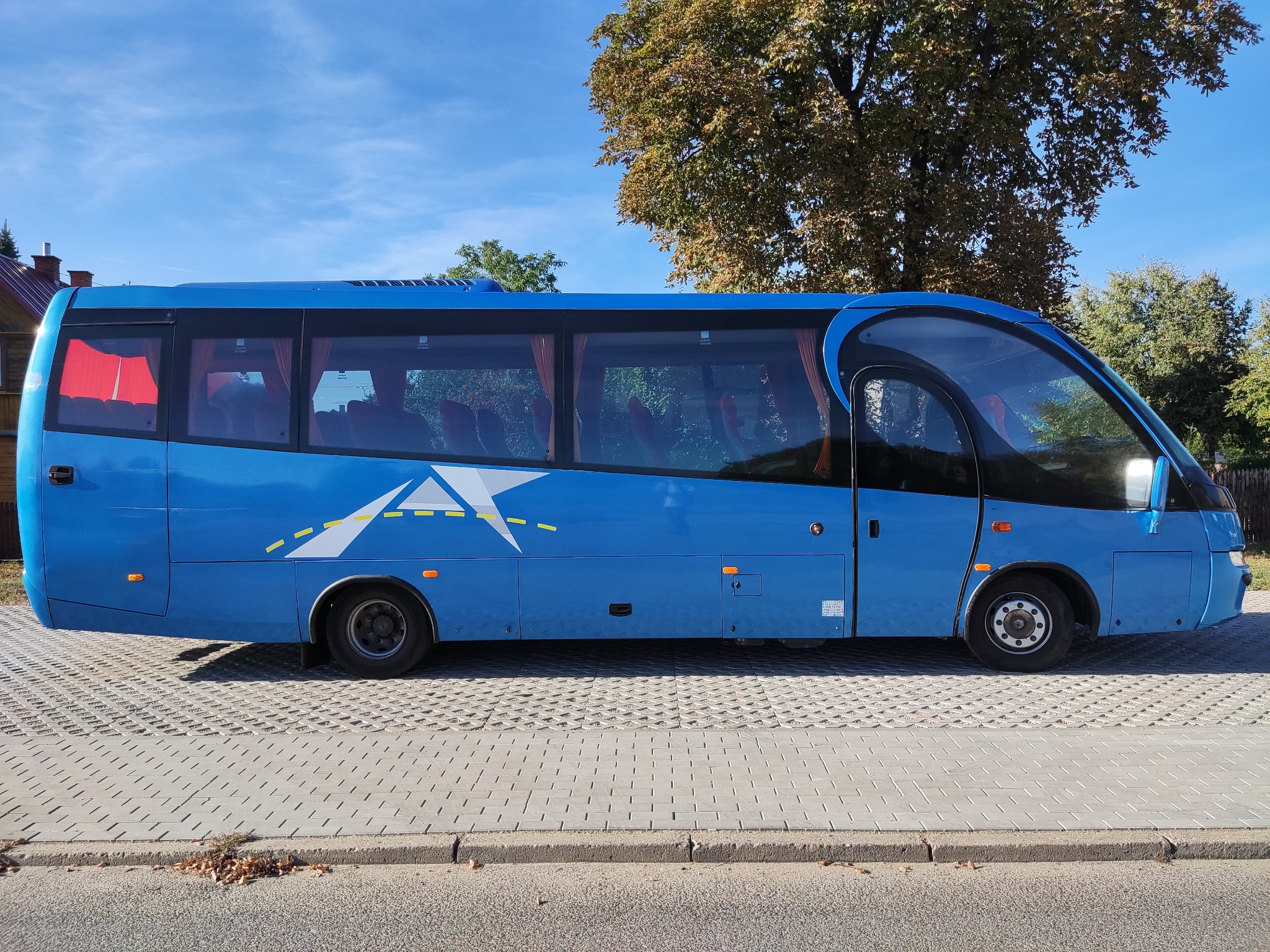 Niebieski autobus turystyczny z grafiką gwiazdy na tle błękitnego nieba i drzew