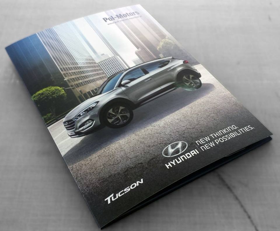 Zdjęcie przedstawia otwartą teczkę z nadrukiem samochodu Hyundai Tucson na tle miejskiego krajobrazu z wieżowcami, logo firmy Pol-Motors widoczne w górnej części teczki.