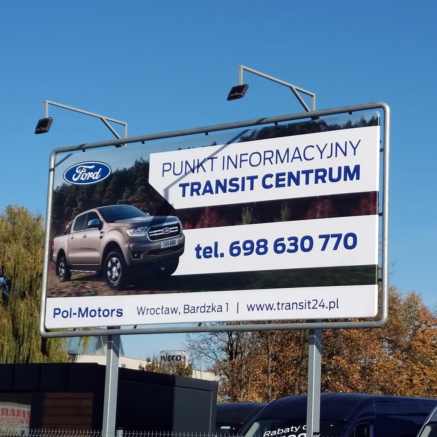 Billboard reklamowy Ford Transit Centrum z beżowym Fordem Rangerem na tle jesiennego krajobrazu, widoczny numer telefonu i adres strony internetowej.