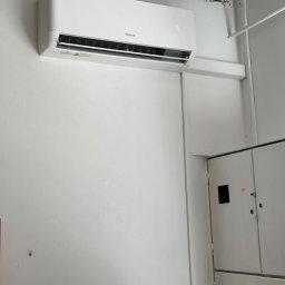 Sunsat - Biały klimatyzator marki Mistral zamontowany na białej ścianie w pomieszczeniu biurowym, obok rozdzielnicy elektrycznej.