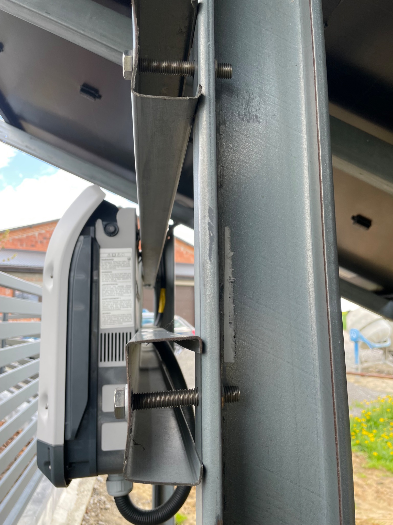 Szczegół mocowania falownika do metalowej konstrukcji wsporczej paneli słonecznych, widoczne śruby i elementy złączne.