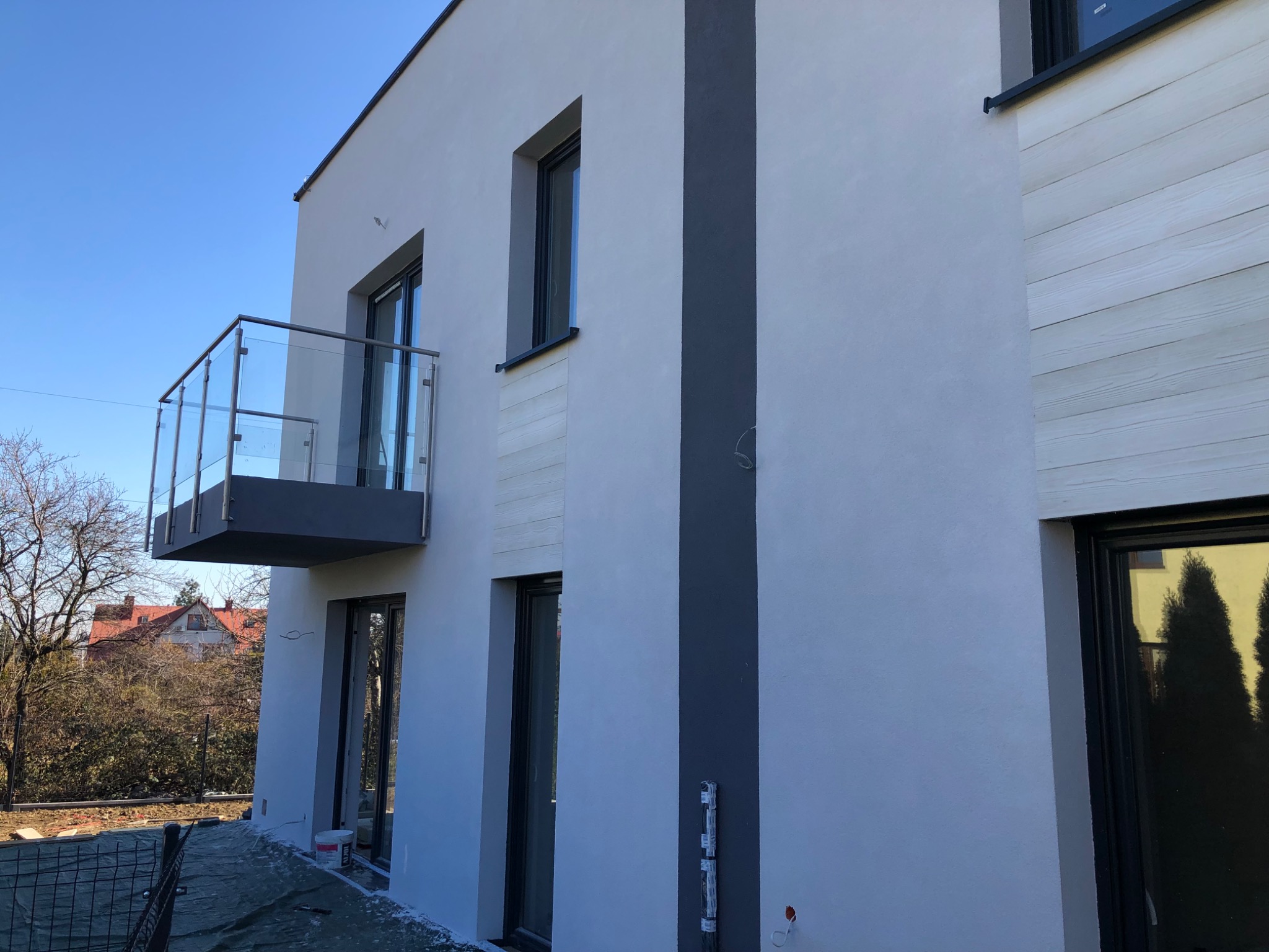 Elewacja budynku po remoncie w Siemianowicach Śląskich, widoczne gładkie ściany w odcieniach szarości, okna z czarnymi ramami, szklany balkon oraz fragment drewnianej okładziny.