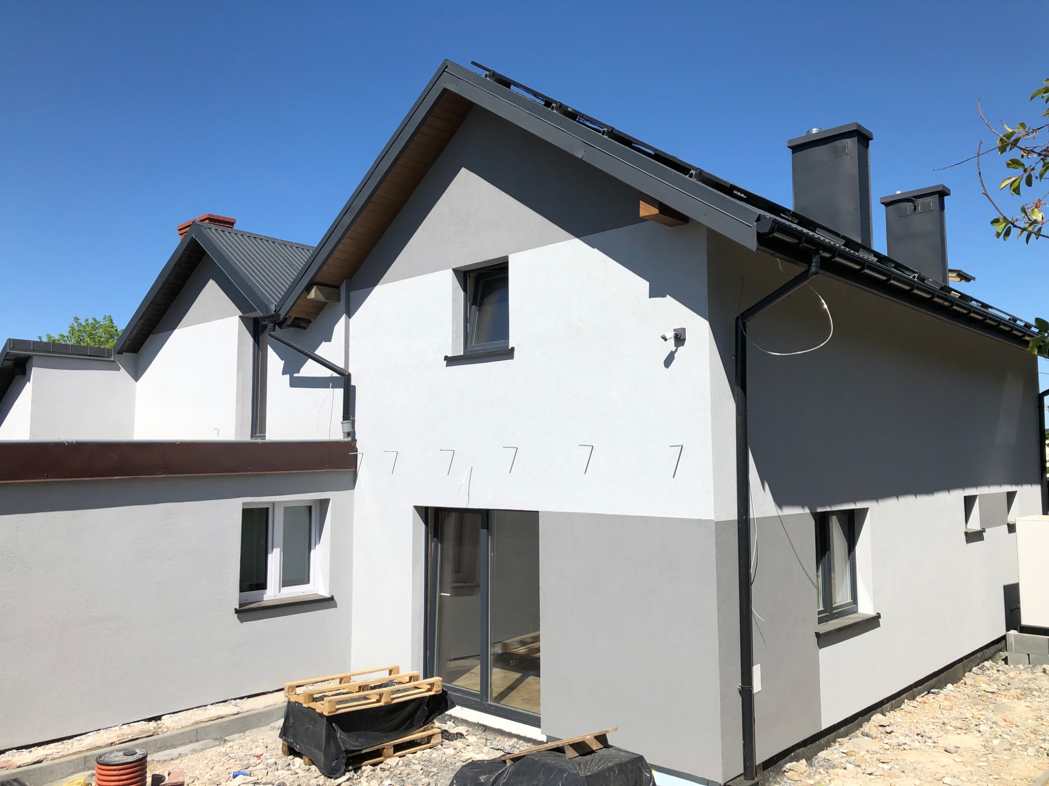 Elewacja dwukondygnacyjnego domu w odcieniach szarości i bieli, z widocznymi elementami wykończeniowymi i przygotowaniami do dalszych prac.