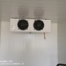 Biała chłodnica przemysłowa z dwoma wentylatorami, zamontowana wewnątrz chłodni z panelami warstwowymi, widoczne miedziane rurki.