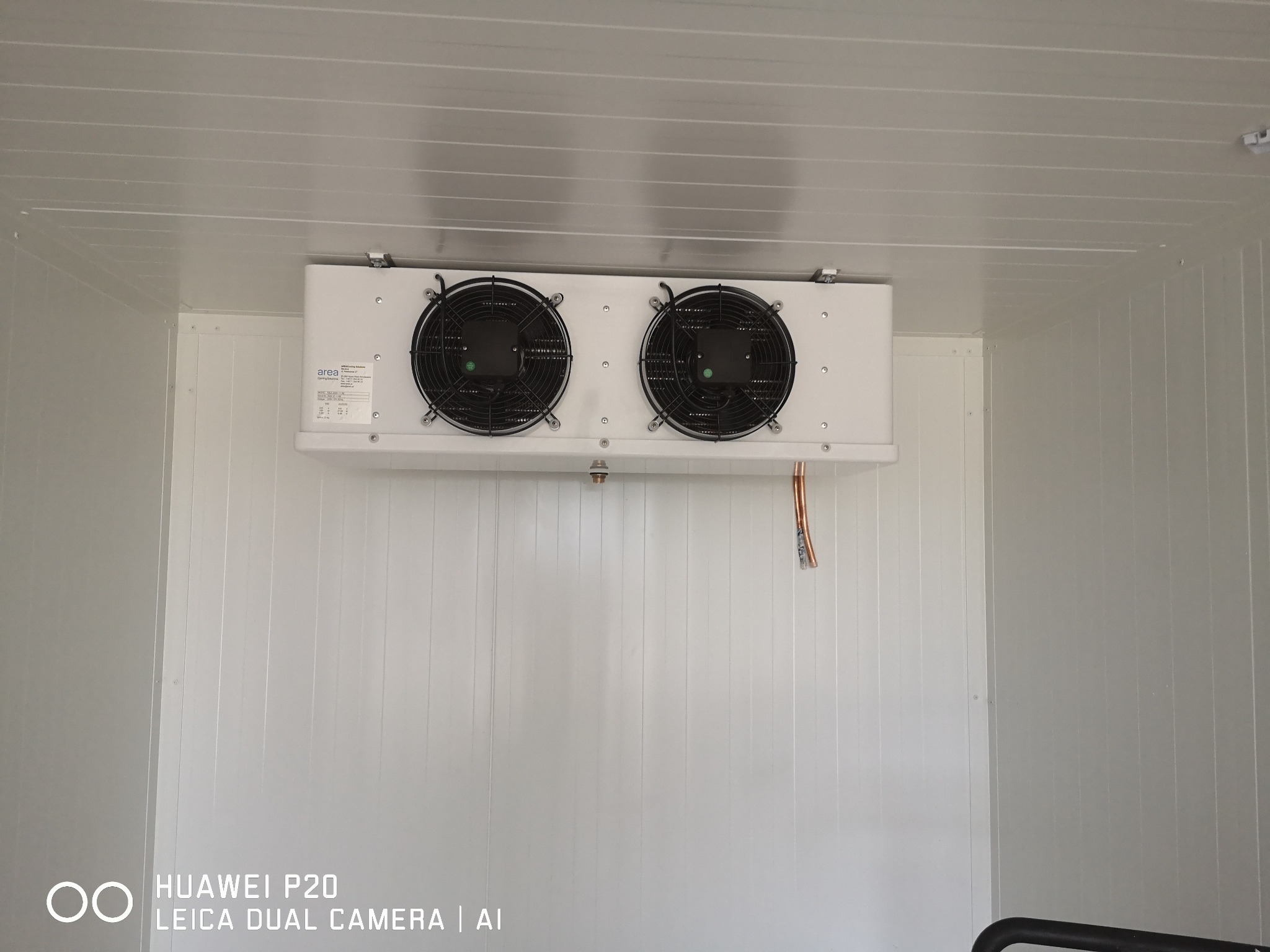 Biała chłodnica przemysłowa z dwoma wentylatorami, zamontowana wewnątrz chłodni z panelami warstwowymi, widoczne miedziane rurki.