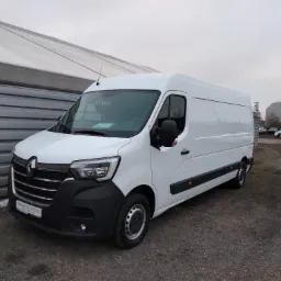 Biały Renault Master, nowy, stojący na placu z szarym żwirowym podłożem, widok z przodu i boku, z budynkiem w tle.