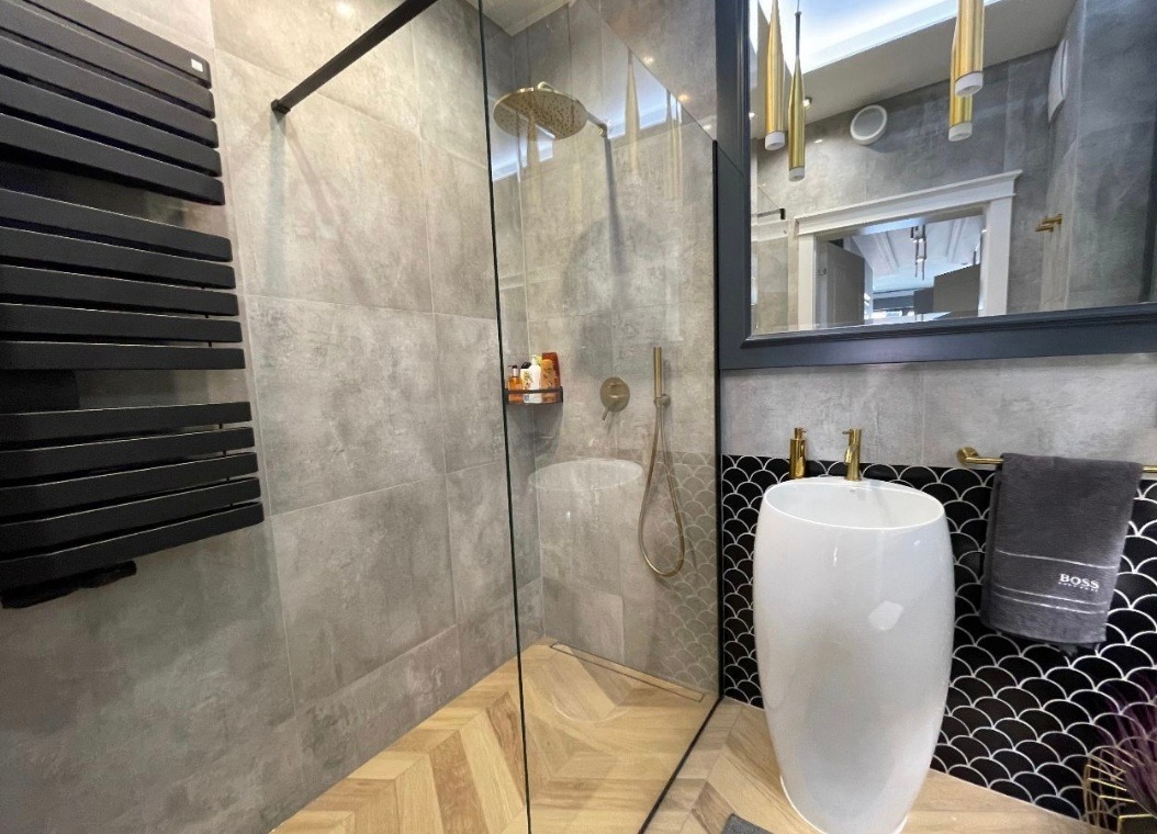 Nowoczesna łazienka z kabiną prysznicową typu walk-in, grzejnikiem drabinkowym w kolorze czarnym, umywalką wolnostojącą i lustrem z dekoracyjnym oświetleniem.
