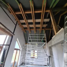 Szkielet drewniany ocieplenia poddasza z widoczną folią paroizolacyjną, rusztowaniem i oknami dachowymi w nowym domu.