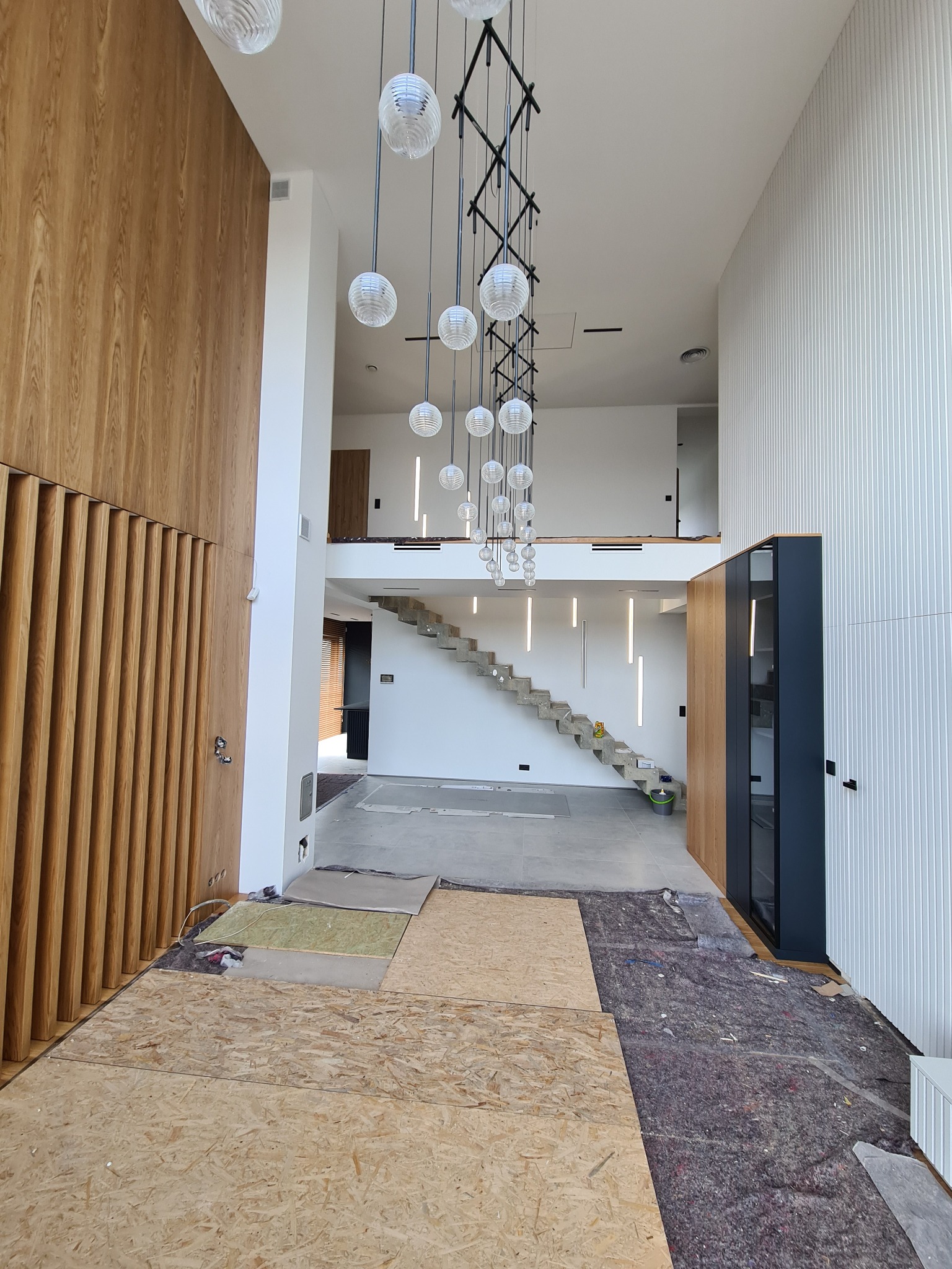 Wnętrze domu w trakcie układania podłogi, widoczne płyty OSB i materiał izolacyjny na posadzce, w tle schody i nowoczesne oświetlenie.