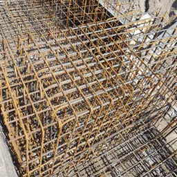 Siatka zbrojeniowa ułożona w szalunku fundamentowym, widoczne zardzewienia na prętach i piasek w tle.