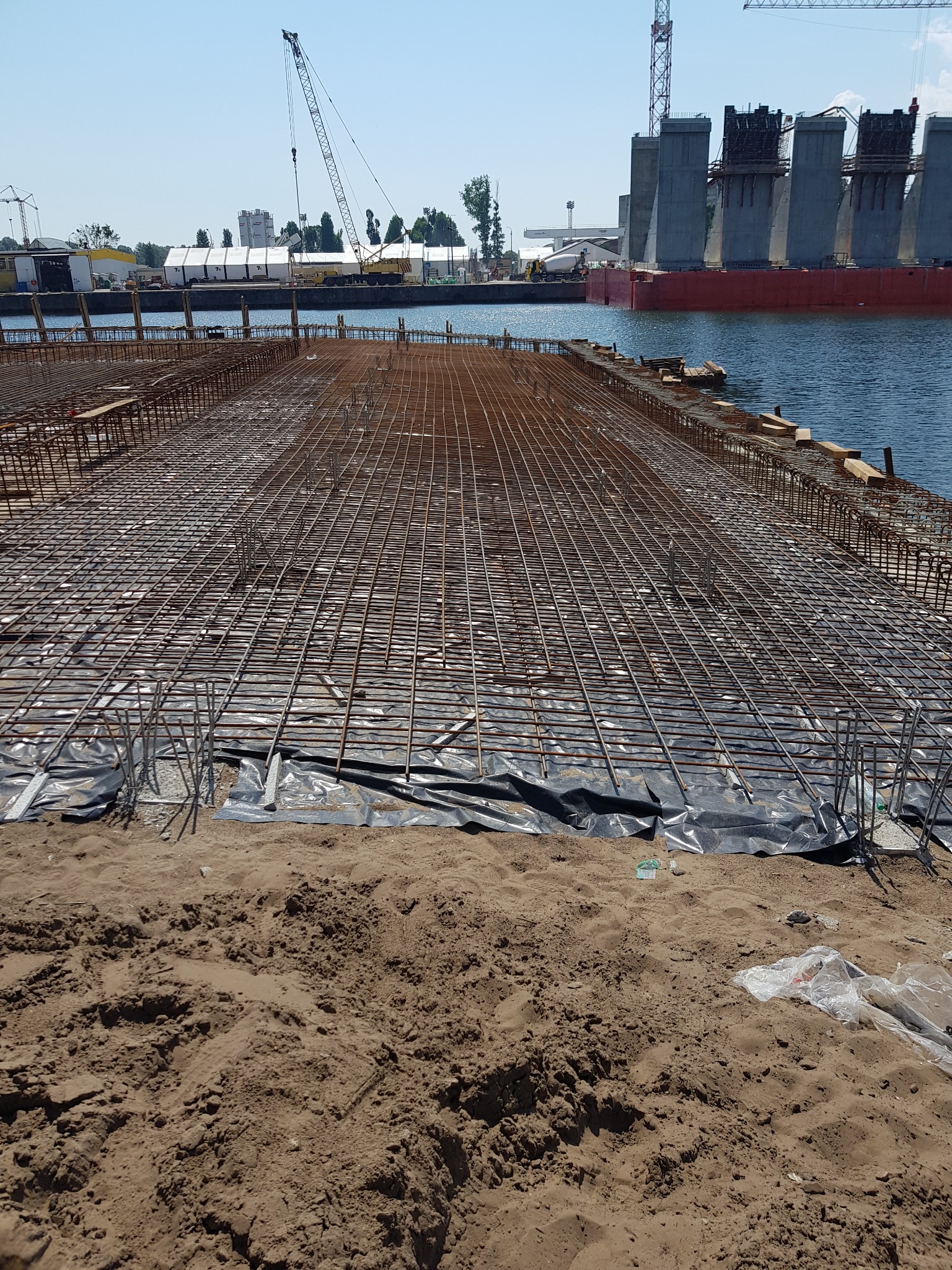 Siatka zbrojeniowa przygotowana do zalania betonem na nabrzeżu, widoczne elementy konstrukcji portowej w tle.