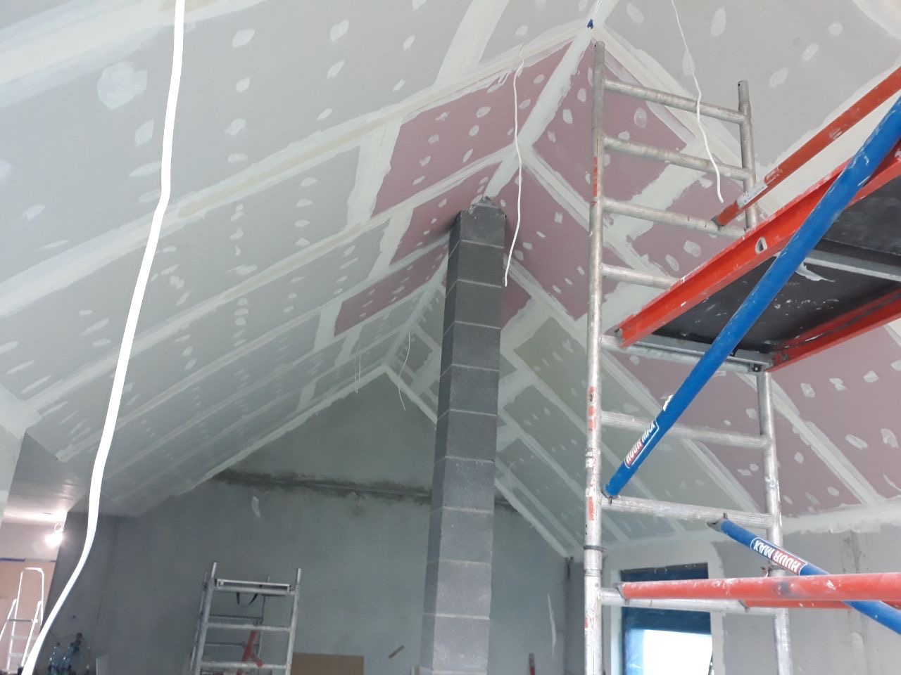 Skośny sufit poddasza w trakcie szpachlowania w Gdyni, widoczne rusztowanie i komin w surowym stanie.