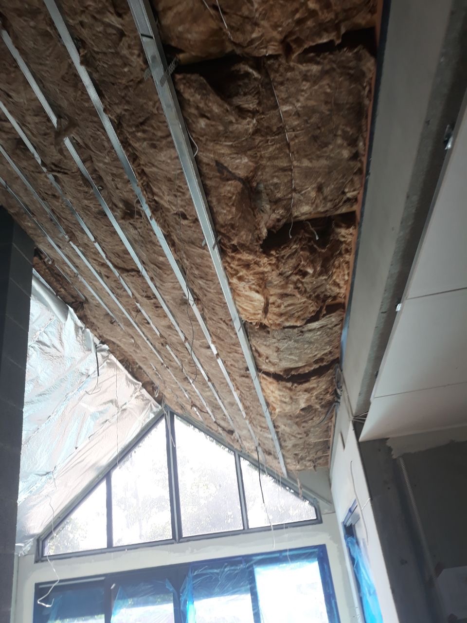 Skośny sufit poddasza w trakcie ocieplania wełną mineralną, widoczne profile metalowe i okno trójkątne.