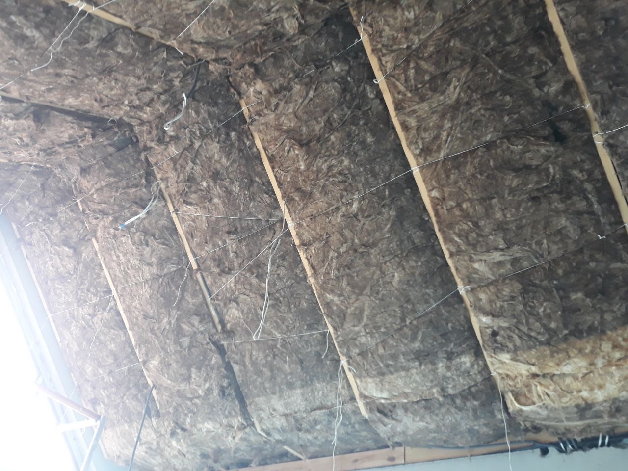 Izolacja poddasza z widocznymi belkami drewnianymi i przewodami elektrycznymi, zabezpieczona drutem